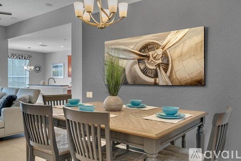A dining room with a wooden table and chairs, a chandelier, and a large painting on the wall.