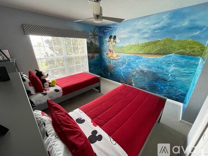 A room with a wall mural of a beach scene and a red bed.