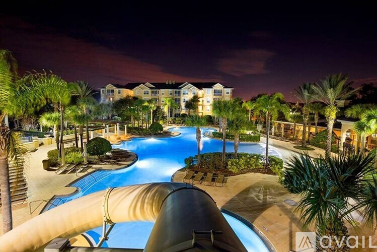 A pool area at night with a slide and a building in the background.