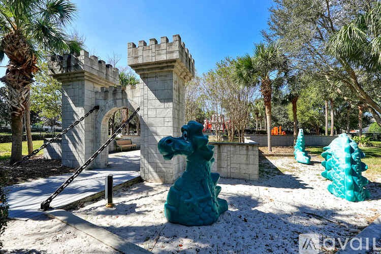 A blue dragon statue is in the foreground of a park with a castle-like structure in the background.