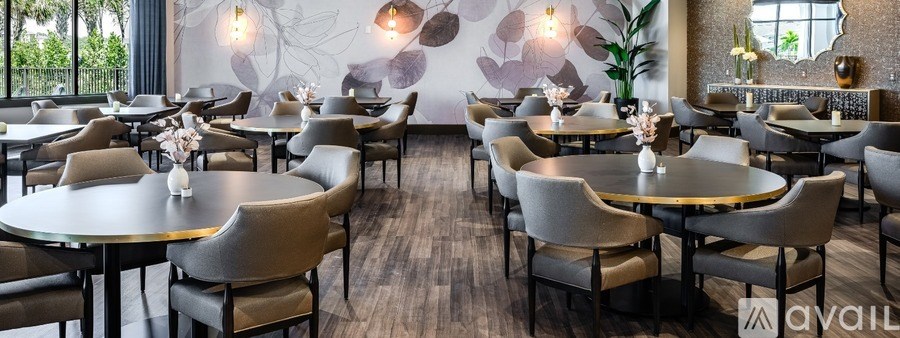 A restaurant with round tables and chairs, a vase of flowers on the table, and a wall with a floral design.