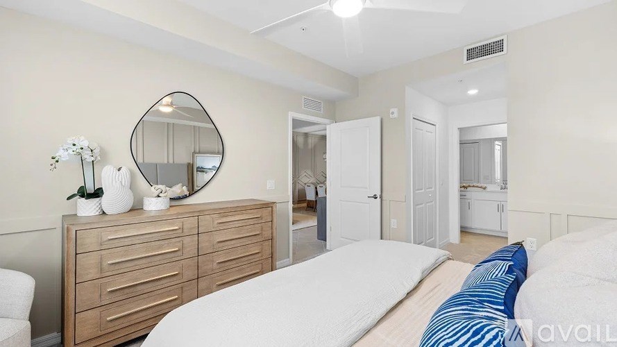 A bedroom with a white bed and a wooden dresser with a mirror above it.
