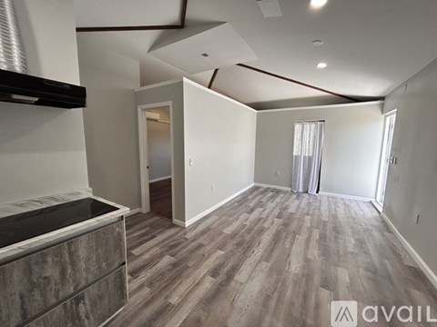 A room with wooden flooring and a kitchen area with a counter and cabinets.
