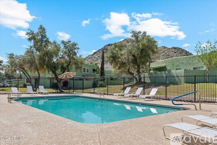 A pool surrounded by chairs and trees with a house in the background.