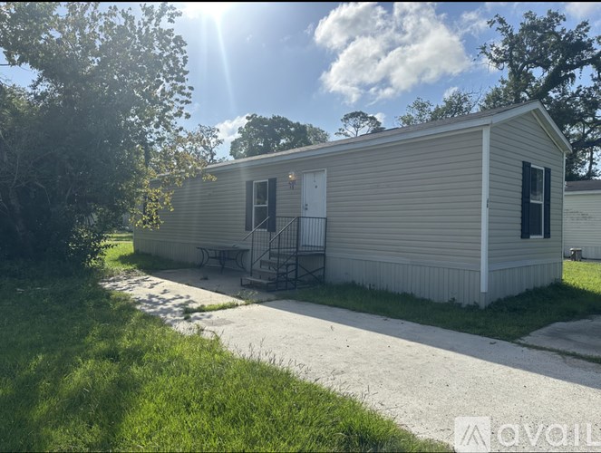 A mobile home with a porch and a small tree in front.
