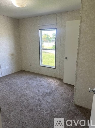 A room with a carpeted floor and a window overlooking a green area.