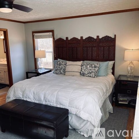 A bedroom with a large bed and a black ottoman.