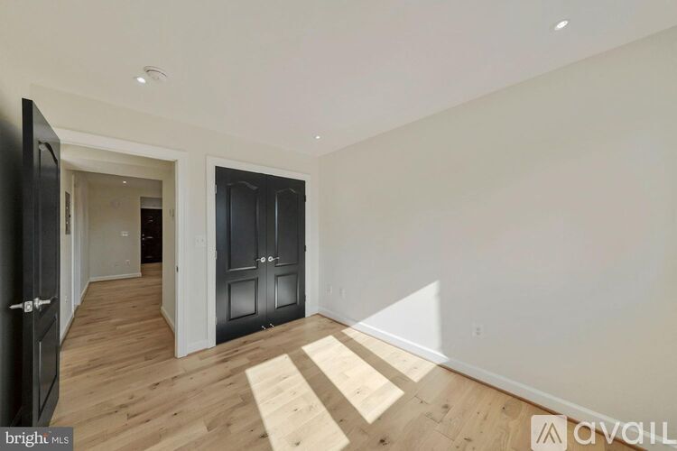 A room with wooden flooring and white walls, with a black wardrobe and a white door.