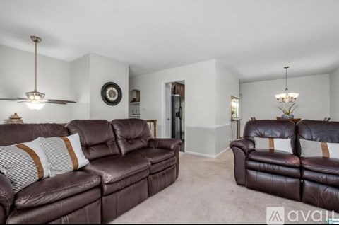 A living room with a brown leather couch and a chandelier.