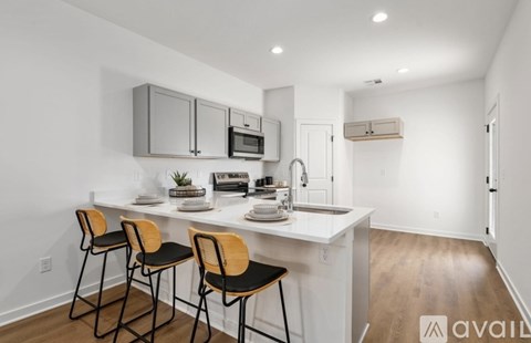 A kitchen with white cabinets and a white countertop with a sink and two chairs.
