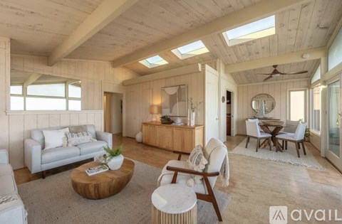 A spacious living room with a skylight, a white sofa, a wooden coffee table, and a dining area with a round table and chairs.