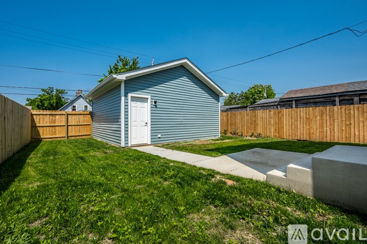 A small blue house with a white door is surrounded by a wooden fence and a grassy yard.