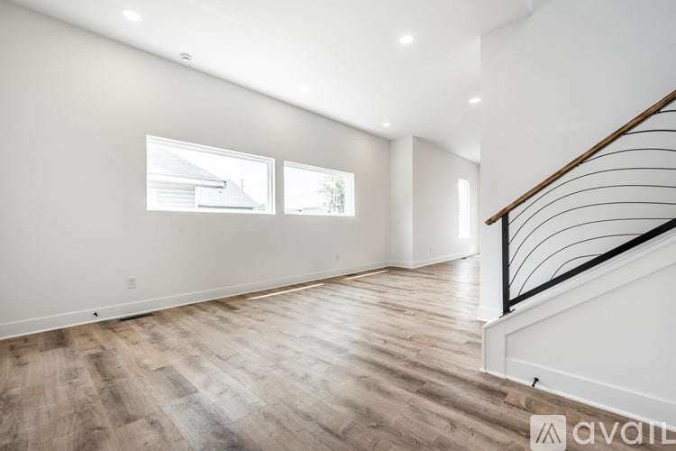 A spacious room with wooden flooring and a staircase with a black railing.
