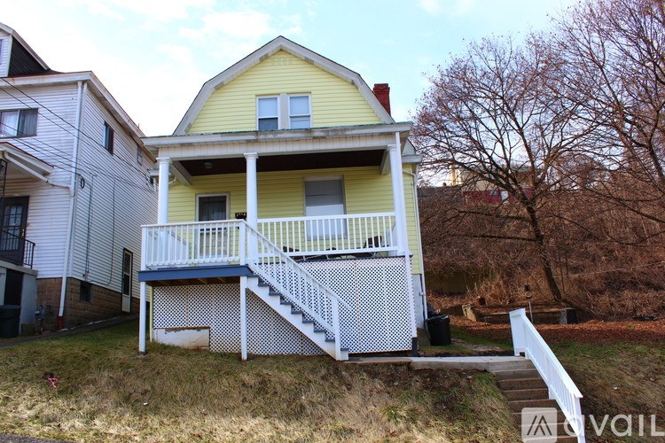 A yellow house with a white porch and stairs.