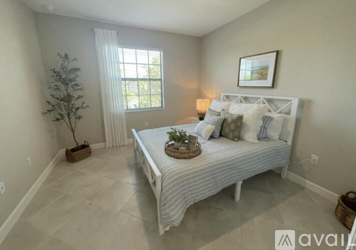 A bedroom with a bed, pillows, a plant, and a picture on the wall.