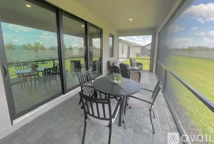 A patio with a table and chairs is shown with a view of a grassy area and a building in the distance.