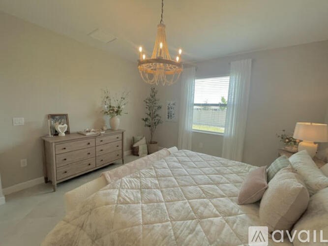 A bedroom with a large bed, a chandelier, and a dresser with a mirror.