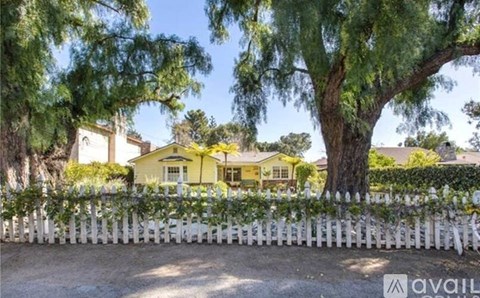 A yellow house is surrounded by a white picket fence and trees.