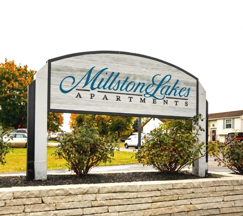 A sign for Millstone Lakes Apartments is displayed in front of a grassy area.