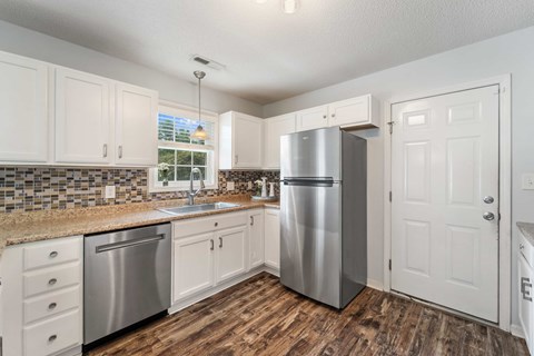 A kitchen with a stainless steel refrigerator and wooden floors.