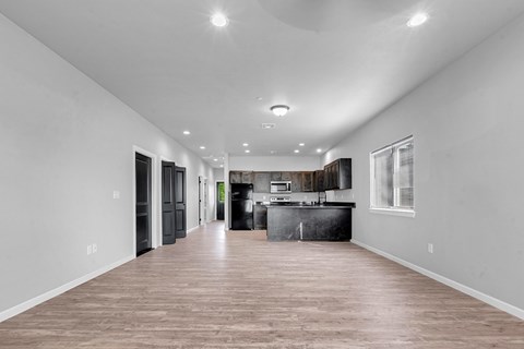 A spacious kitchen and living room with hardwood floors and white walls.
