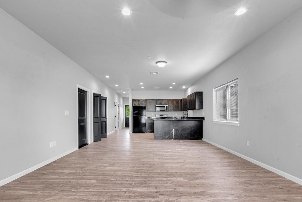 A spacious kitchen and living room with wood flooring and white walls.