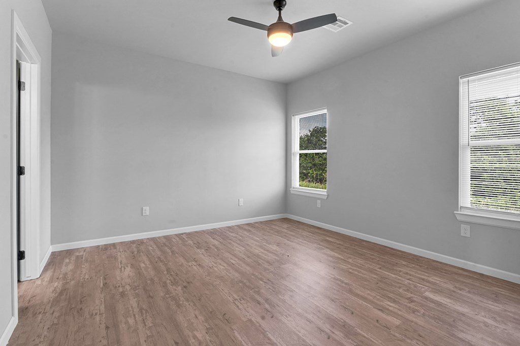 A room with a ceiling fan and light, hardwood floors, and a window with blinds.
