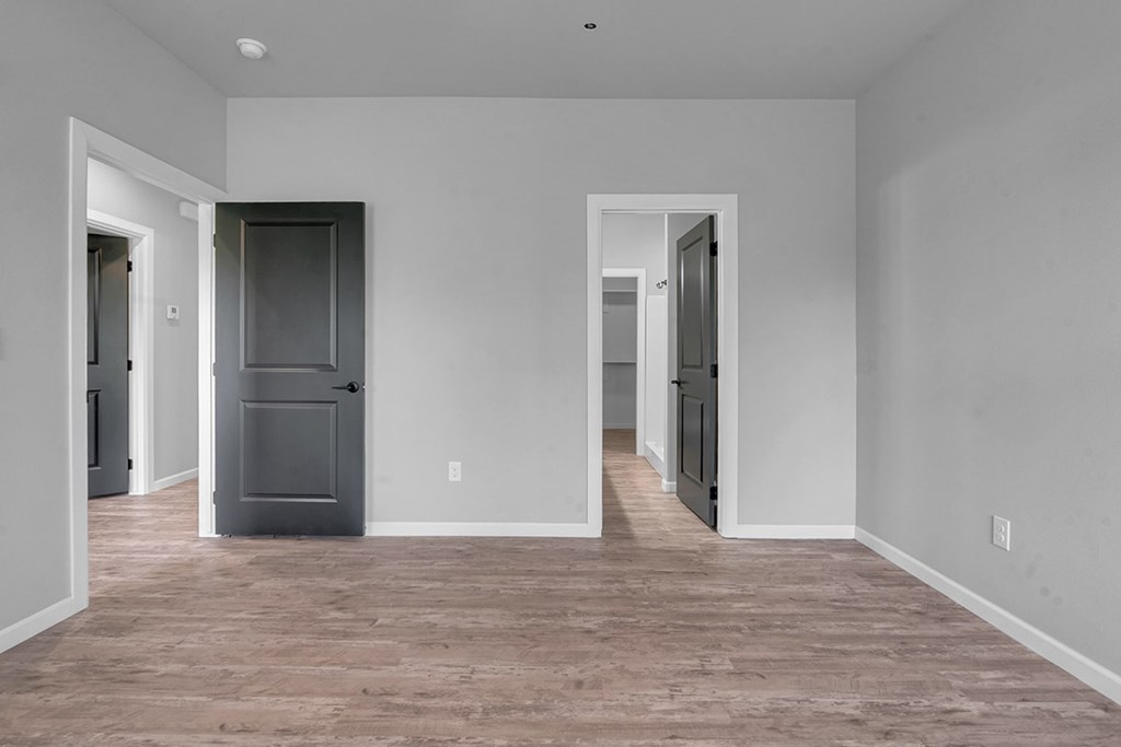 A room with a grey fridge and wooden flooring.