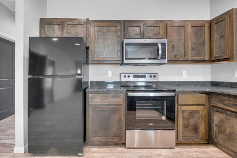 A kitchen with a black refrigerator, stainless steel oven, and microwave above a stainless steel counter.