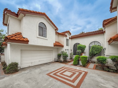 A white house with a red tile roof and a driveway with a patterned border.