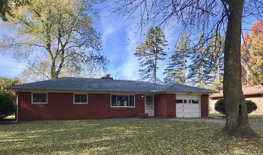 A red house with a white garage door and a tree in front.