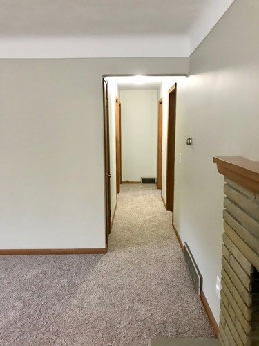 A hallway with a carpeted floor and a wooden railing on the right side.