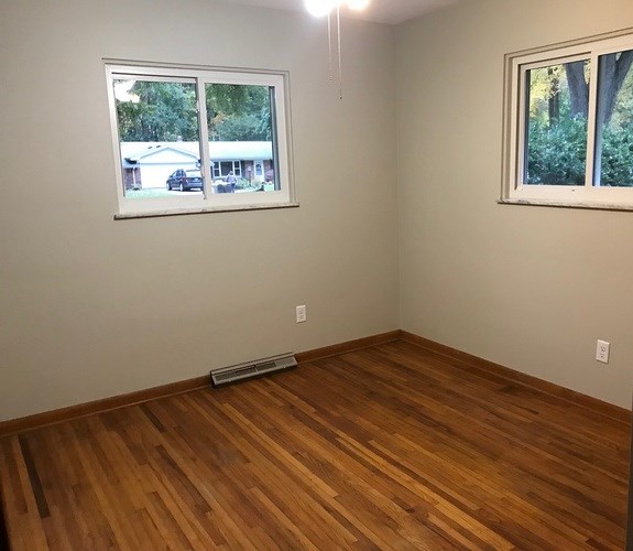 A room with wooden flooring and two windows.