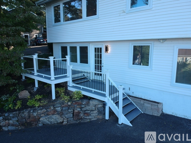 A white house with a deck and a stone wall.
