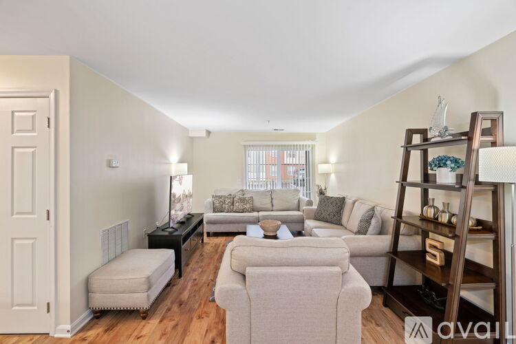 A living room with a white door, a grey couch, a black coffee table, and a wooden shelf with decorative items.