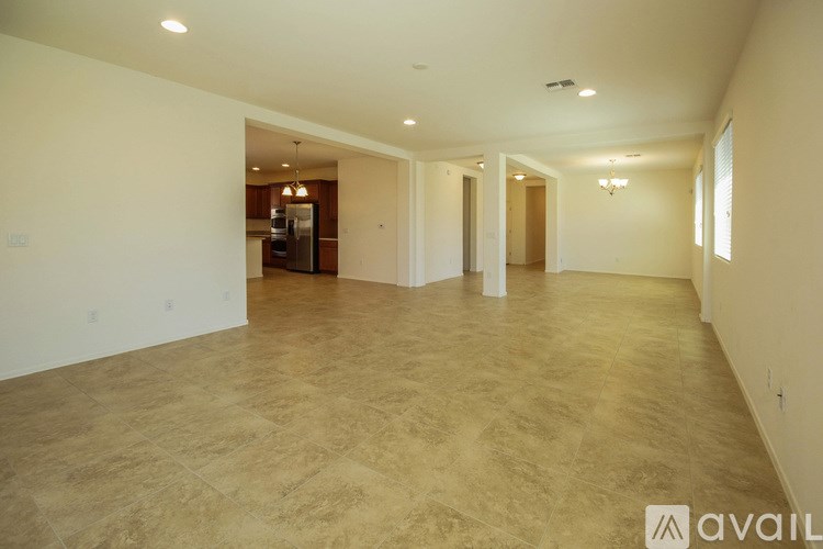 A spacious room with beige carpeting and a kitchen visible through the open door.