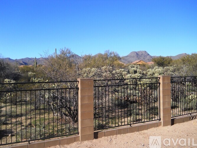 A black metal fence with a brick pillar separates a grassy area from a mountainous background.