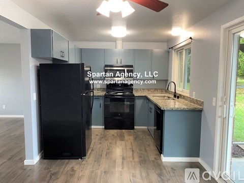 A kitchen with a black fridge and a window with a view of the grass.