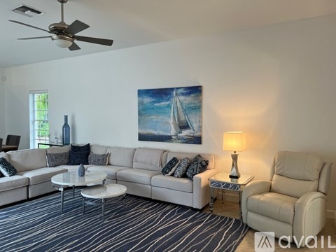 A living room with a white couch, a painting of a sailboat, and a ceiling fan.