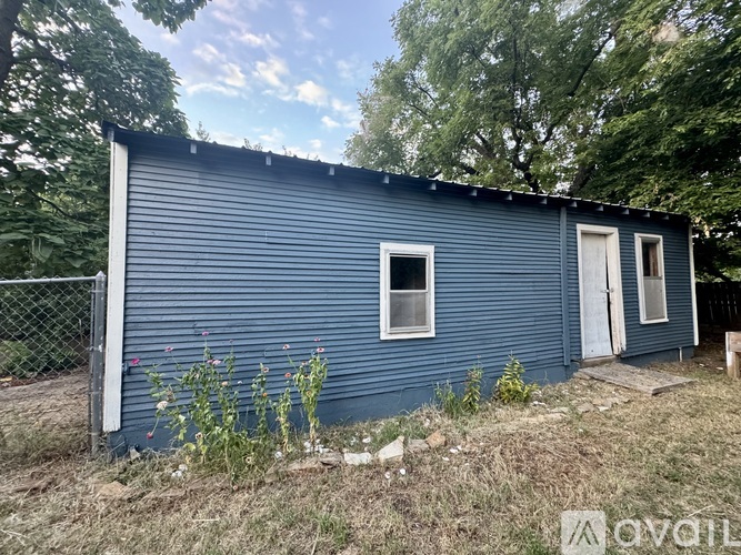 A blue house with a white door and windows surrounded by trees.