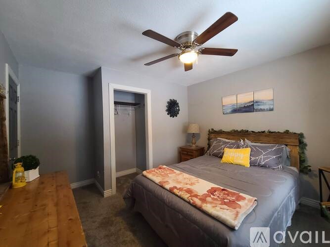 A bedroom with a bed, a ceiling fan, and a painting on the wall.