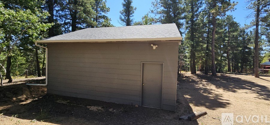A small building with a grey door is surrounded by trees.