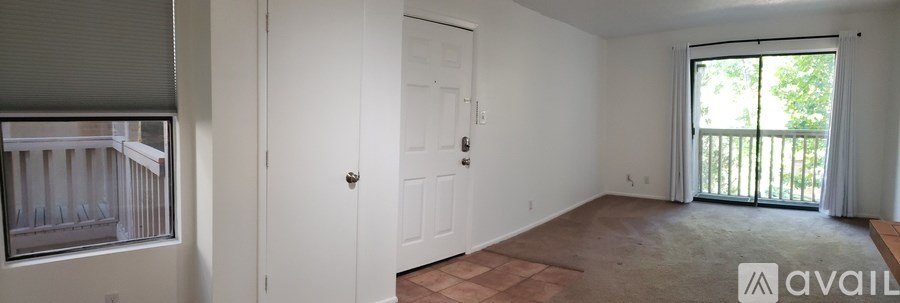 A room with a door, a window with blinds, and a balcony with a railing.