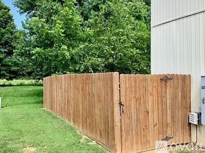 A wooden fence in front of a green lawn and a white building.