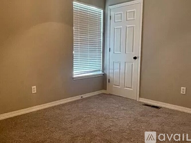 A room with a carpeted floor, a door, and a window with blinds.