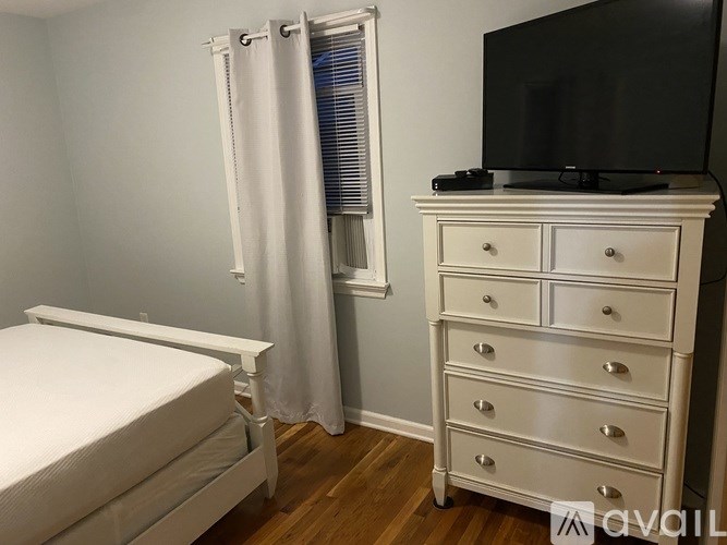 A white bedroom with a bed, dresser, and television.