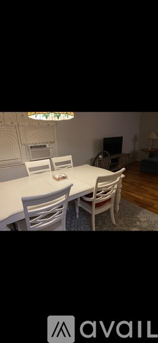 A white dining table with four chairs and a television in the background.