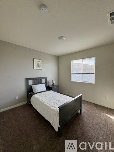 A bedroom with a bed, carpet, and a window.