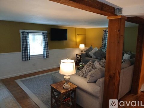 A living room with a grey couch, a wooden table with a lamp, and a flat screen TV mounted on the wall.