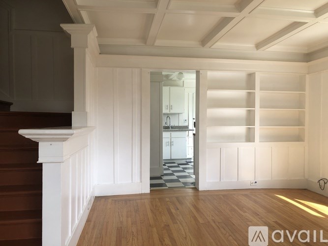 A room with wooden floors and white walls with a staircase on the left side.